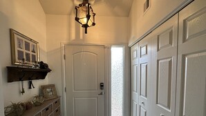 Un pasillo con una puerta blanca, suelo de madera y un estante en la pared con objetos decorativos.