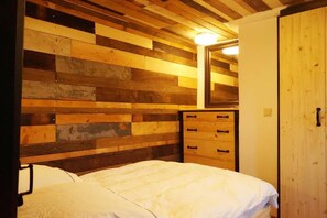 A bedroom with a wooden headboard, a bed with white bedding, a dresser with drawers, and a wooden door.