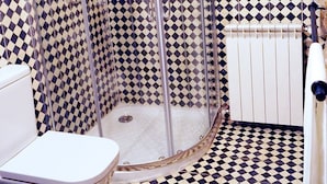 Une salle de bain avec un carrelage à motifs géométriques, un espace douche, des toilettes et une fenêtre avec une plante.