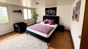 Un dormitorio con cama, mesita de noche, cómoda, ventana y una planta.