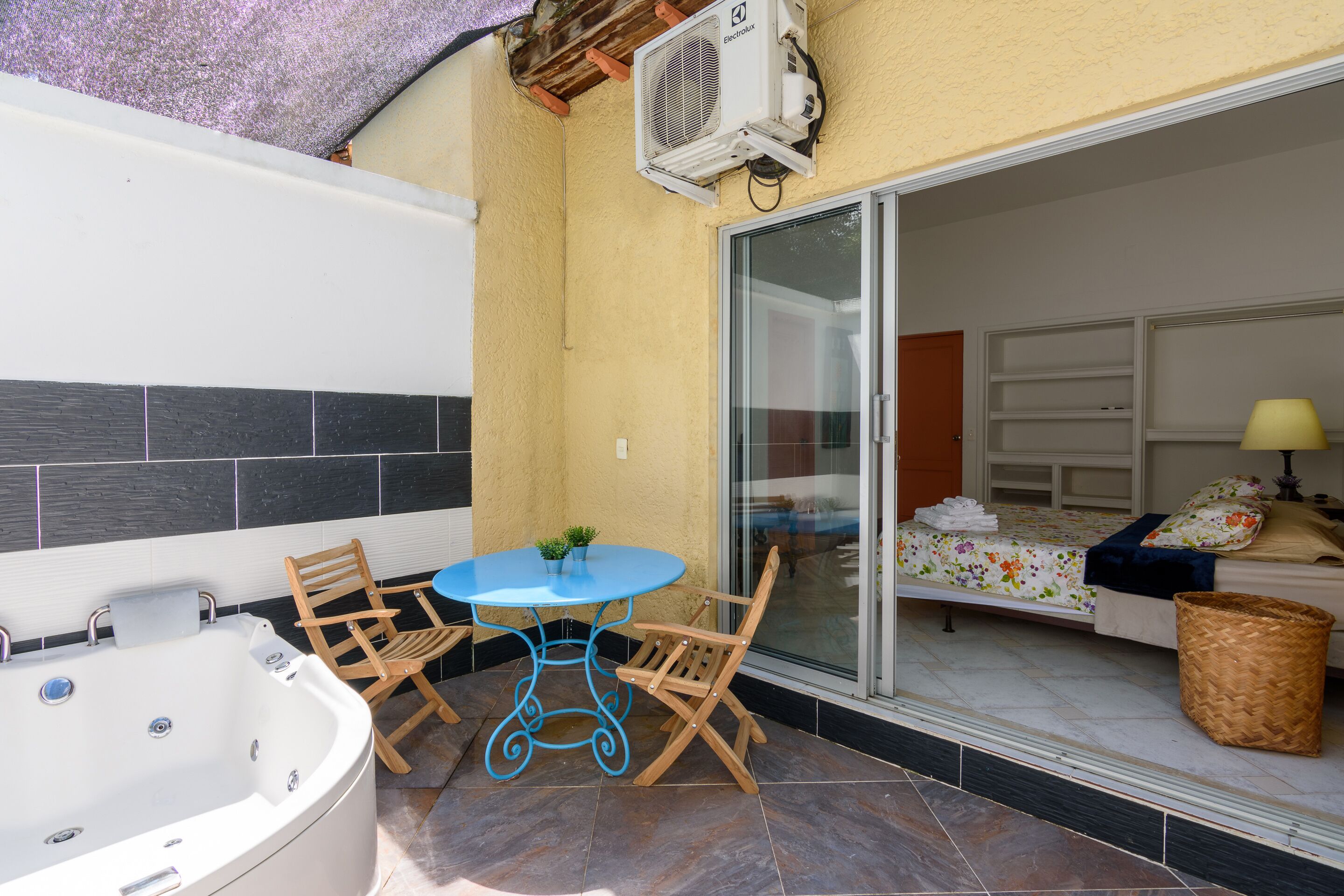 A balcony with a hot tub, a table with chairs, and a bed with a window.