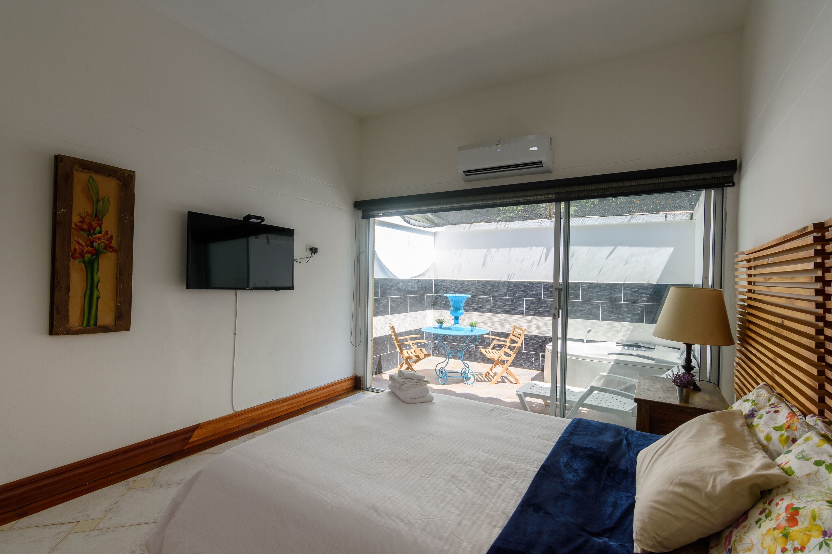 A bedroom with a bed, a television mounted on the wall, a window with a view of the outside, and a small table with chairs.