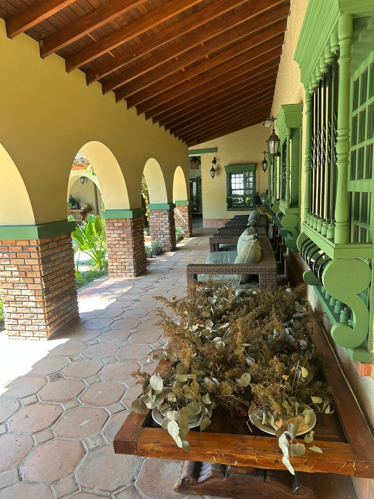 A covered patio area with brick pillars, green window frames, and a planter with dried plants.