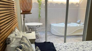 Un dormitorio con cama, mesita de noche, lámpara colgante y vistas a un área exterior con jacuzzi y mesa.