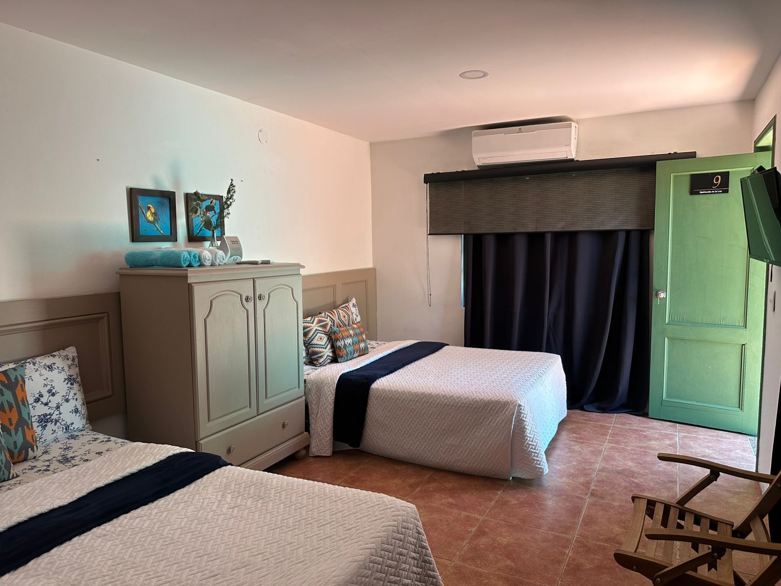 Habitación de hotel con dos camas, un armario, un escritorio y una puerta verde.