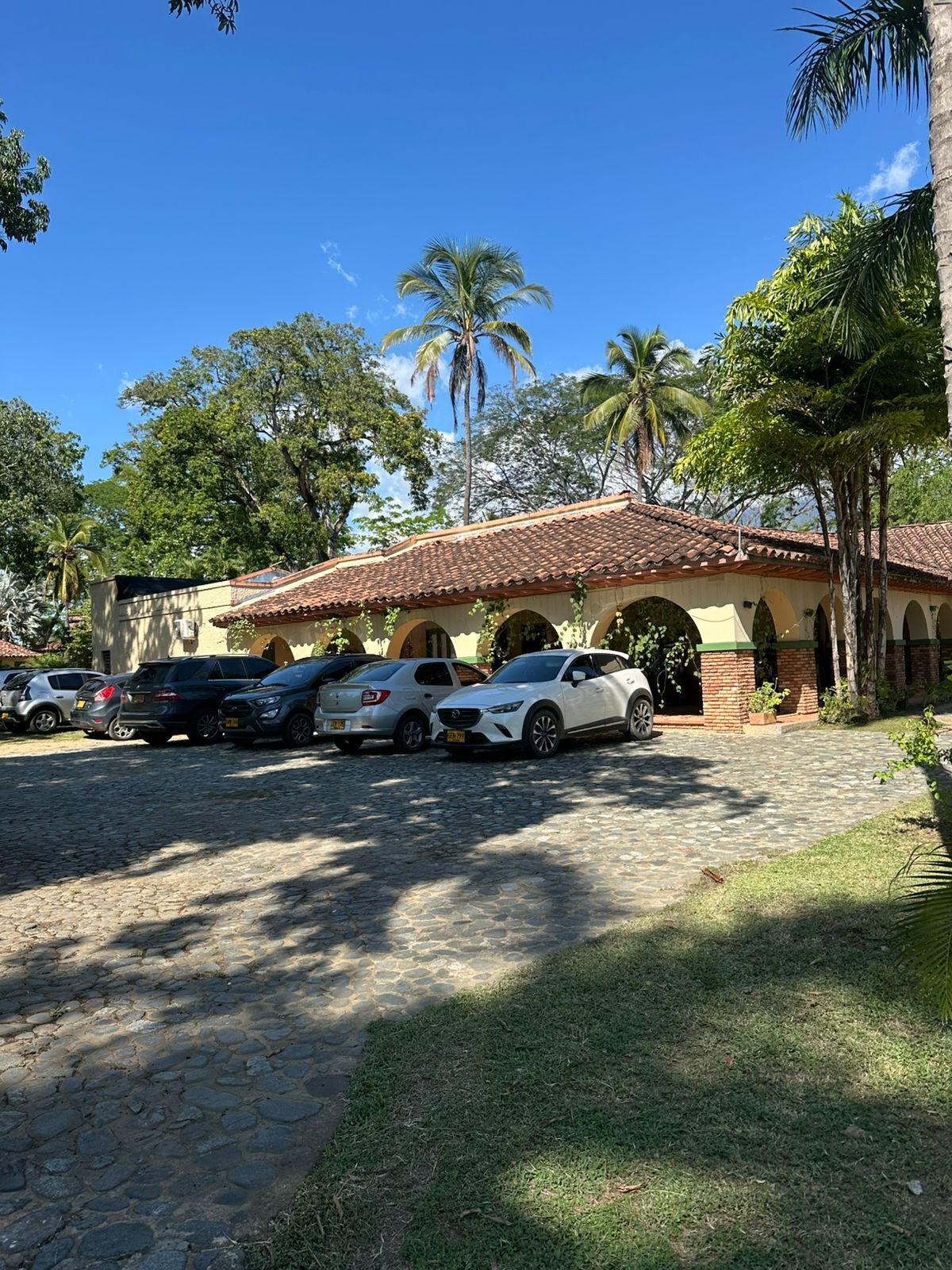 A building with a tiled roof and arched windows, surrounded by parked cars and palm trees.