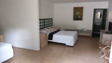 Habitación de hotel con cama, escritorio, silla, mesita, espejo y un cuadro en la pared.