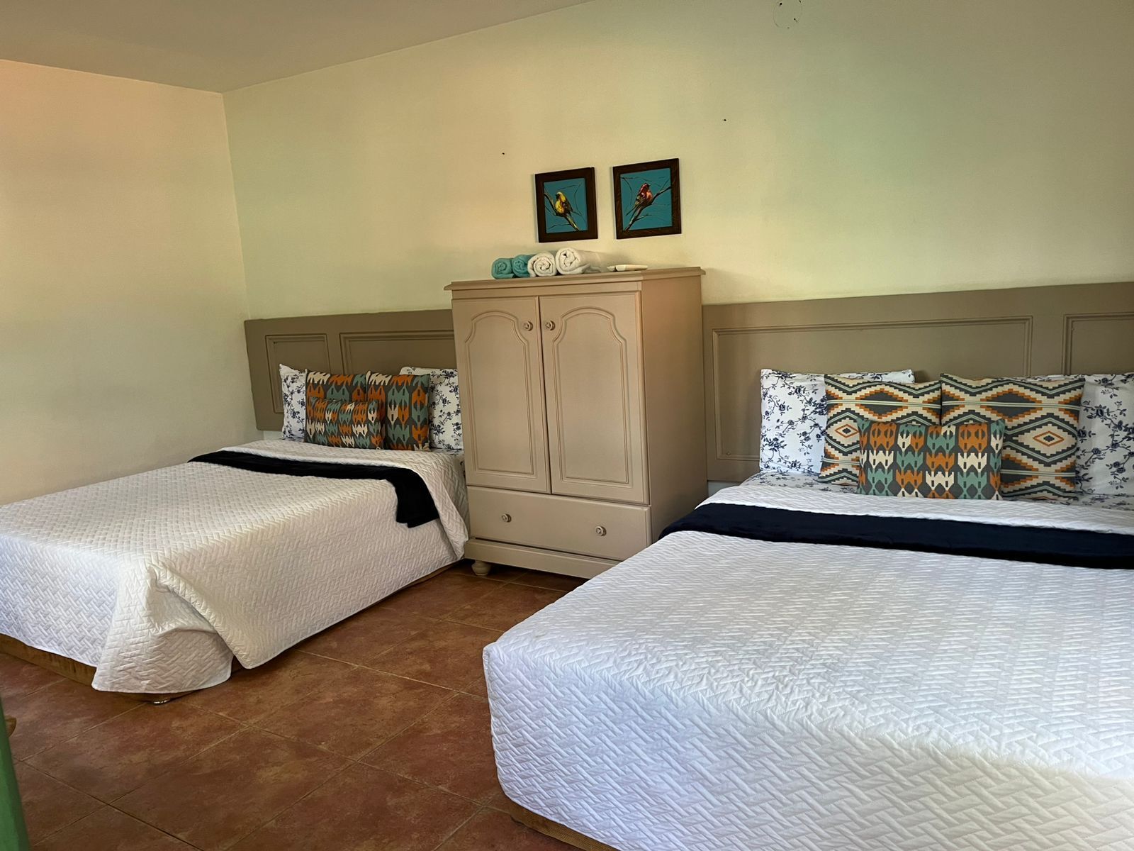 Une chambre d’hôtel avec deux lits, une armoire et deux tableaux accrochés au mur.