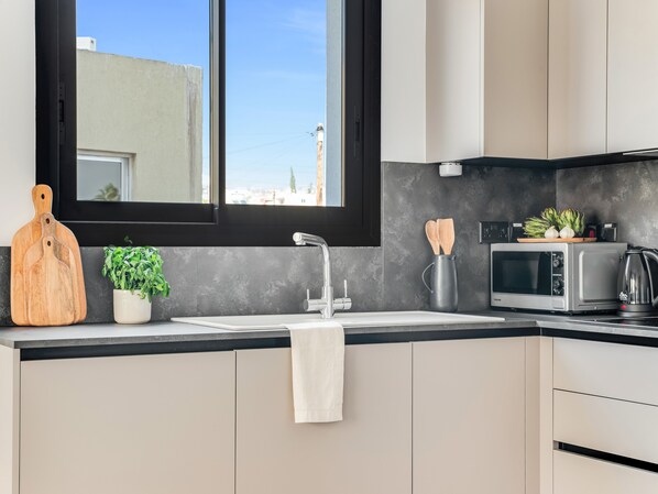 Een moderne keuken met een groot raam, een spoelbak, een magnetron en een waterkoker.