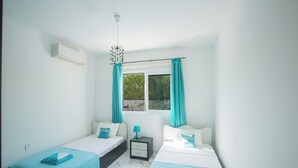 A hotel room with two beds, a window with curtains, a nightstand, and an air conditioning unit. - Protaras Holiday Villa Gd44 (Paralimni)