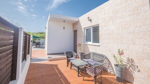 A patio with a wooden deck, a table with chairs, a potted plant, and a building with a stone facade. - Protaras Holiday Villa Gd44 (Paralimni)