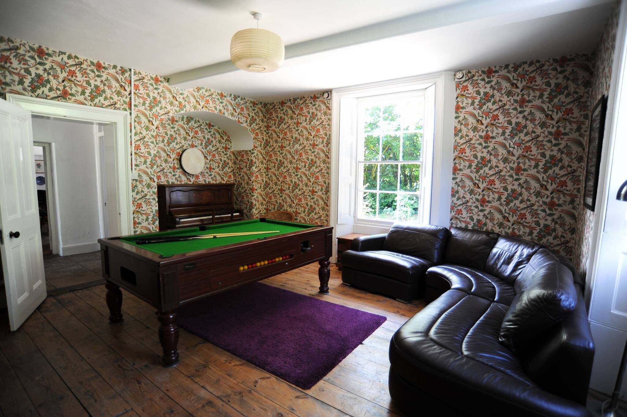 A room with a pool table, a leather sofa, and floral wallpaper.