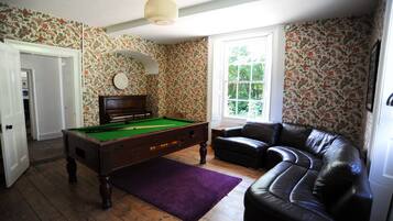 A room with a pool table, a leather sofa, and floral wallpaper.