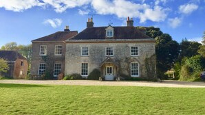 A large, two-story stone building with a symmetrical facade, a central entrance with a door and windows, and a small balcony on the upper floor. - Manor House Moreton - Entire Holiday Home (Dorchester)