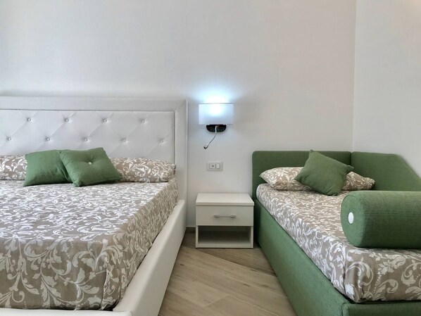 A bedroom with two beds, a nightstand, and a wall-mounted light. - Trifoglio Apartment in S Pietro (Maiori)