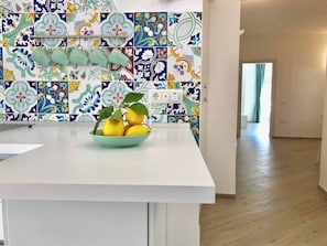 A kitchen with a white countertop, a bowl of lemons, and a tiled backsplash with floral patterns. - Trifoglio Apartment in S Pietro (Maiori)