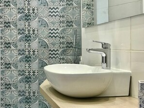 A bathroom with a white sink, chrome faucet, and patterned tile backsplash. - Trifoglio Apartment in S Pietro (Maiori)
