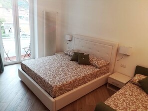 A bedroom with a bed, bedside tables, a radiator, and a view through a sliding door. - Trifoglio Apartment in S Pietro (Maiori)