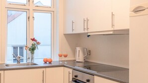 A modern kitchen with white cabinets, a black and white checkered floor, a window with flowers, and a kettle on the counter. - Charming House Close to Everything (Aarhus)