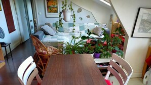 A cozy room with a wooden dining table, wicker chairs, a bed with a checkered quilt, and several potted plants. - If you Like it, Stay If you Dont Like it, Just Stay (Hanoi)