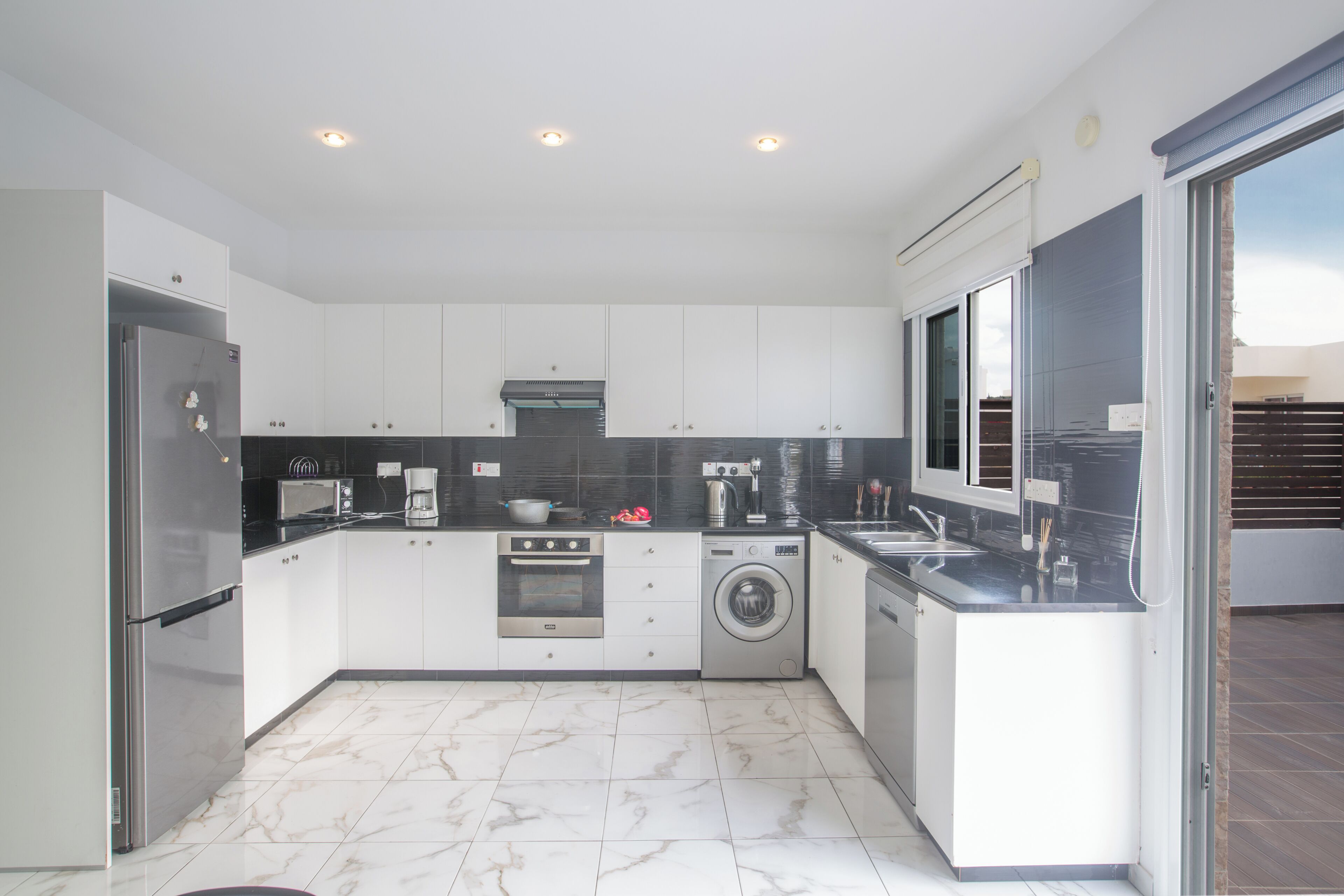 A modern kitchen with white cabinets, stainless steel appliances, a built-in oven, microwave, and washing machine.
