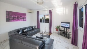 Ein modernes Wohnzimmer mit einem grauen Ledersofa, einem Couchtisch und einem Flachbildfernseher auf einem Standfuß.