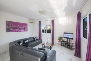 A modern living room with a grey leather sofa, a coffee table, and a flat-screen TV on a stand. - Protaras Holiday Villa Gd42 (Paralimni)