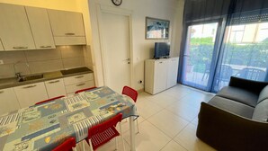 A compact living space with a dining area, kitchenette, and a balcony with a sofa. - Flat With Private Garden by the sea (Caorle)