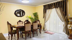A dining room with a round table, six chairs, a mirror, a potted plant, and a large window with curtains. - House w 3 Bedrooms And 3 Baths - Free Parking (Olongapo)