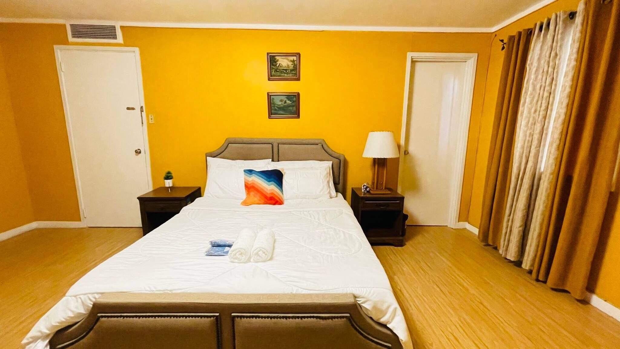 A hotel room with a large bed, two bedside tables, a nightstand, a lamp, and a door.