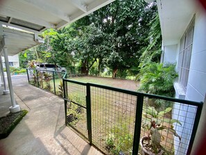 A covered outdoor area with a metal fence, potted plants, and a white car parked nearby.