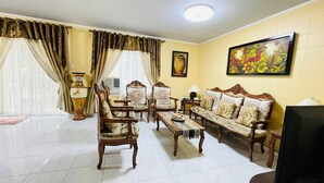 A living room with a sofa set, a coffee table, and a television. There are curtains, a vase, and a painting on the wall. - House w 3 Bedrooms And 3 Baths - Free Parking (Olongapo)