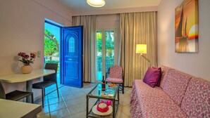 A living room with a sofa, a chair, a coffee table, and a dining table. There is a blue door leading to an outdoor area with greenery. - Bbq, Backyard, Of Amoudara, Full Kitchen, Parking-3 (Malevizi)