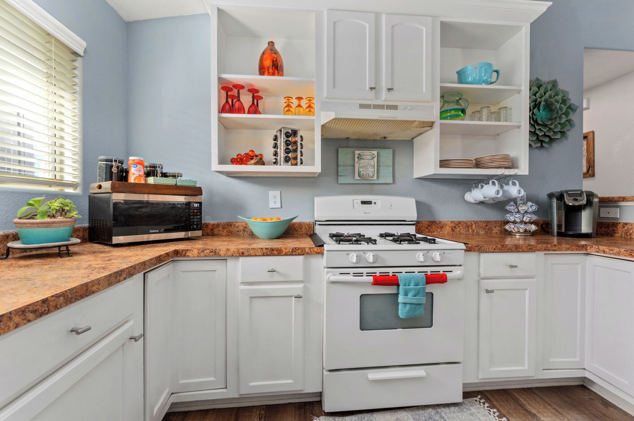 Una cucina con mobili bianchi, piano cottura a gas, forno a microonde e lavandino.