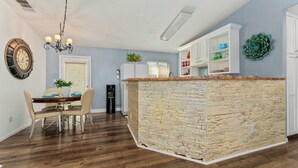 A modern kitchen with a stone island, white cabinetry, and a dining area with a table and chairs. - Casa Luisa Joshua Tree (Joshua Tree)