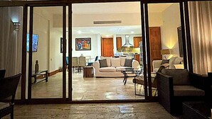 A spacious living area with a large sofa, a coffee table, and a dining table. There is a kitchen area visible in the background. - Srvittinivillas Aptla/ Best View/ Fam/couple/ Team/ Work Tr/ Casa de Campo Rv (La Romana)