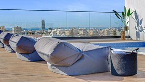 Una terraza en la azotea con piscina, sillas de descanso y una planta en maceta.