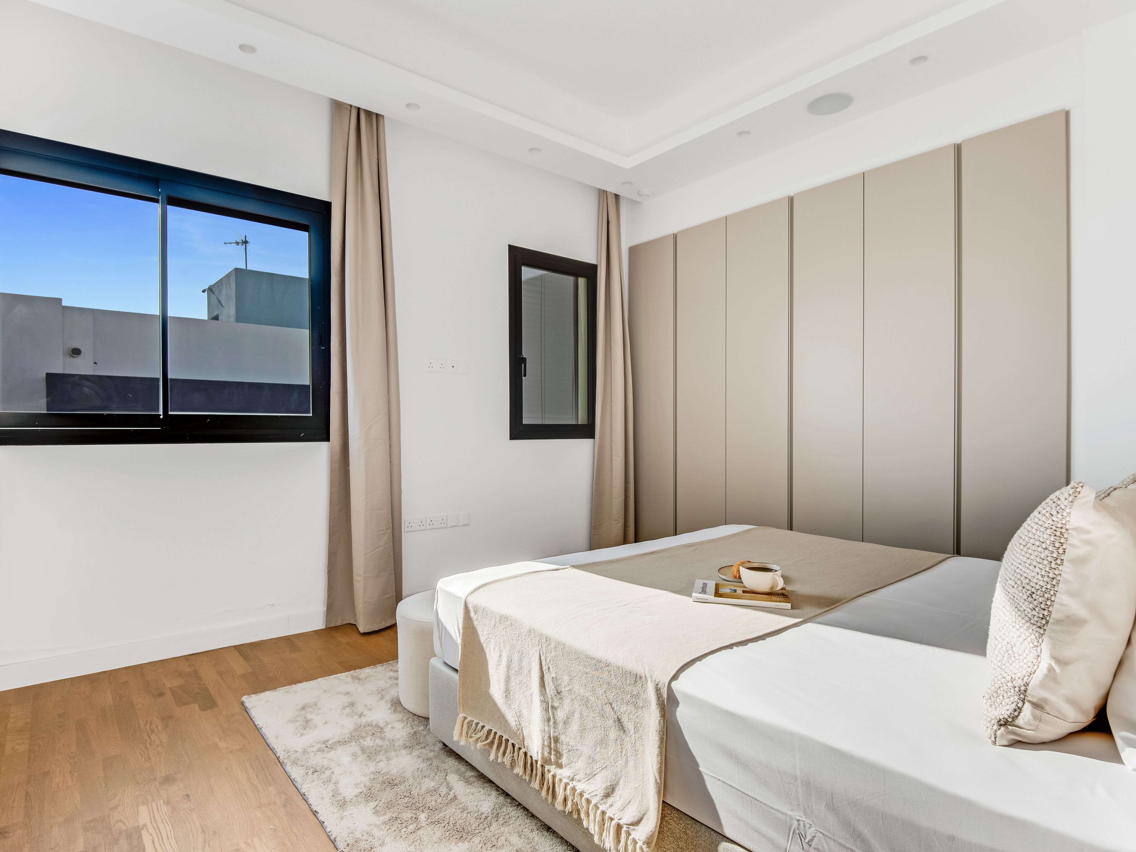 Quarto moderno com uma janela grande, uma cama, uma mesa de cabeceira e um guarda-roupa.