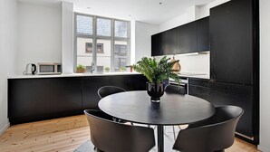 A modern kitchen with black cabinets, a round dining table with four chairs, a potted plant, and a window providing natural light.
