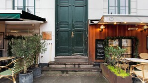 A green double door with a small window above it, a wooden awning, and a signboard with a list of items.