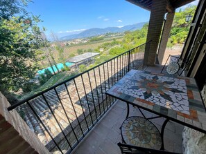 A balcony with a tiled table and chairs, offering a view of a mountainous landscape and a village below. - Apt 2 in Spoleto Stunning Grounds Panoramic Views all Around You! Sleeps 4 (Spoleto)