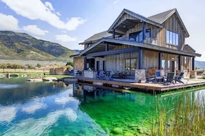 A two-story wooden house with a deck overlooking a clear pool, surrounded by hills. - Abode at Journey's End, hot tub, fire pit, lake access, estate (Kamas)