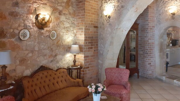 Une pièce chaleureuse avec un mur en pierre, un canapé en bois, un fauteuil à motifs et une petite table sur laquelle est posé un vase de fleurs.