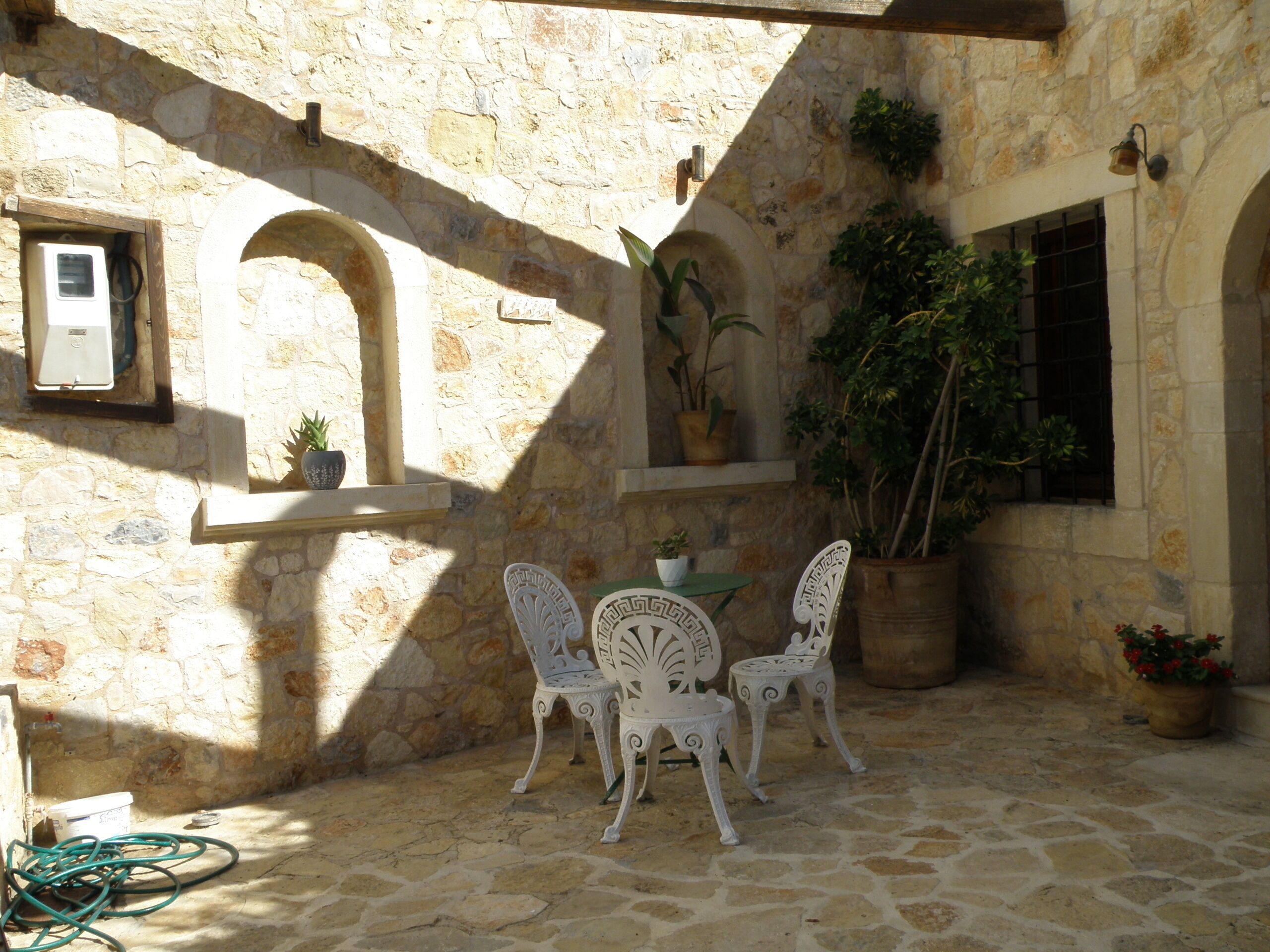 A stone courtyard with a table and chairs, potted plants, and a wall-mounted air conditioning unit.