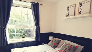 Een slaapkamer met een groot bed, een raam met gordijnen, een bedlampje en twee ingelijste posters met motiverende teksten aan de muur.