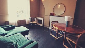 Een kamer met groene gestoffeerde zittingen, een kleine houten tafel met een lamp, een spiegel aan de muur en een radiator.