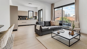 Un salon moderne avec un canapé gris, une table basse et une vue sur la ville grâce à de grandes fenêtres.
