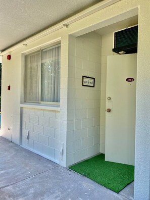A building entrance with a window, a door marked with the number 124, and a small green mat at the entrance.
