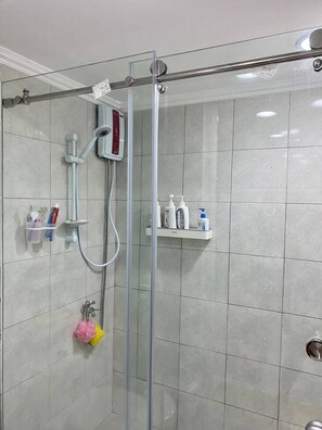 A glass-enclosed shower with a handheld showerhead, a wall-mounted control panel, and a shelf with toiletries.