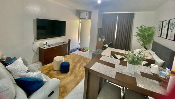 A modern living room with a flat-screen TV, a sofa, a coffee table, and a dining area with a table and chairs. - 1 Bedroom With Free Parking (Morong)